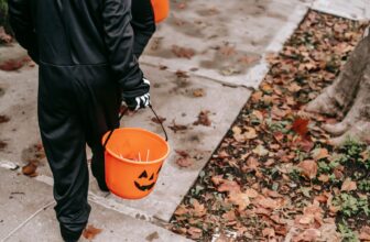 Copii costumați mergând pe trotuar cu găletușe portocalii de Halloween