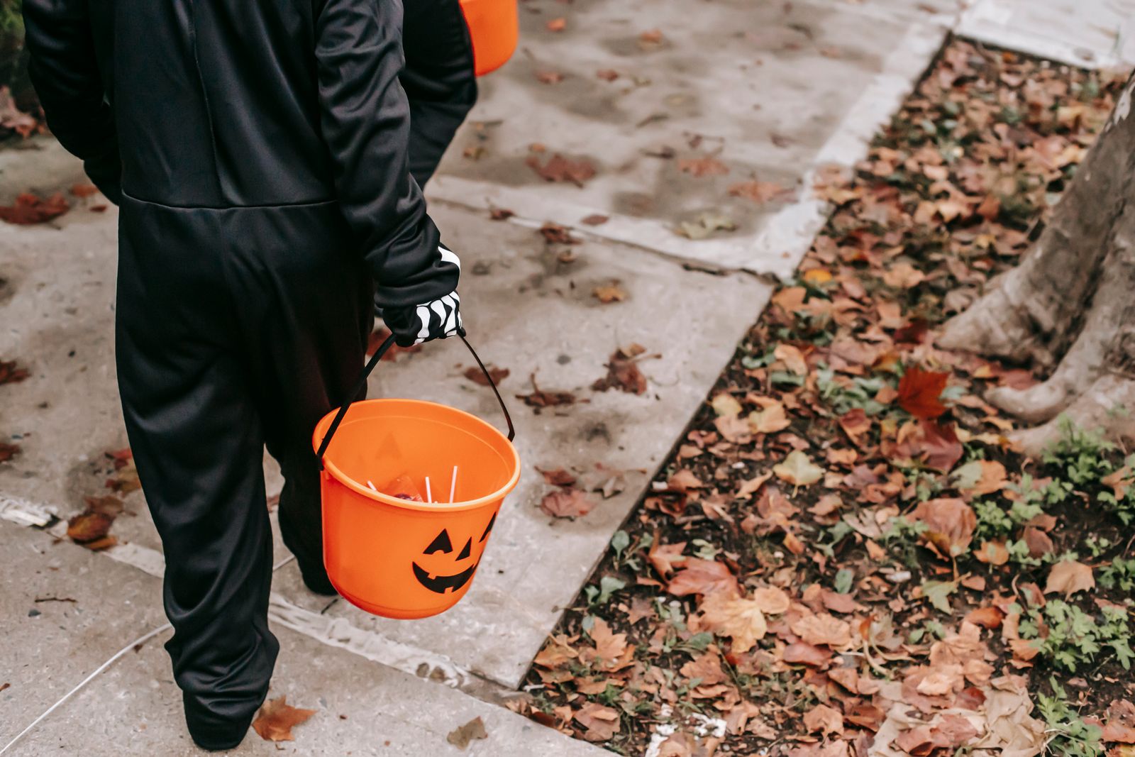 Copii costumați mergând pe trotuar cu găletușe portocalii de Halloween